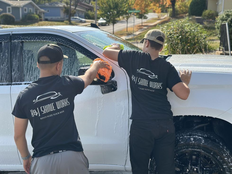 Two K&J Shine Works detailers in branded shirts hand-washing a white pickup truck in a residential driveway